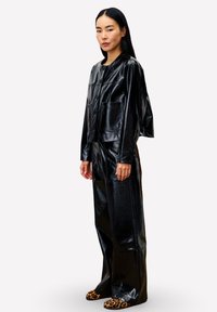 Veste en simili cuir noir avec poches avant, portée avec un pantalon ample assorti et des chaussures à enfiler à imprimé léopard.