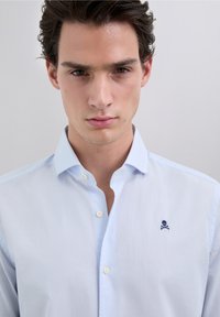 Lichtblauw overhemd met knopen, gemaakt van gestructureerde stof met een klein navy logo van een schedel en gekruiste beenderen op de borst en een klassieke kraag.