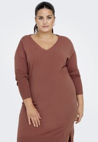 Roestkleurige gebreide jurk met een V-hals, lange mouwen en lichte zijsplitten. Gladde textuur en een relaxte pasvorm.