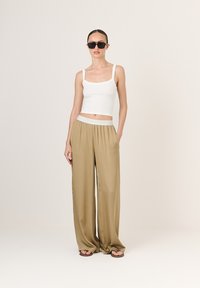 Biely pruhovaný crop top skombinovaný s voľnými béžovými nohavicami. Nohavice majú elastický pás a hladkú, lesklú textúru. Čierne slnečné okuliare dotvárajú vzhľad.