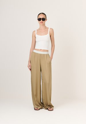 Biely pruhovaný crop top skombinovaný s voľnými béžovými nohavicami. Nohavice majú elastický pás a hladkú, lesklú textúru. Čierne slnečné okuliare dotvárajú vzhľad.