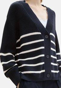 Navyblauer Cardigan mit weißen Streifen, gewebter Textur, V-Ausschnitt und drei schwarzen Knöpfen vorne; lange Ärmel mit gerippten Bündchen.