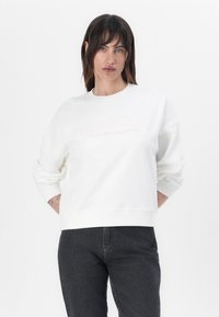 Fehér, pamutból készült pulóver, kerek nyakkivágással és bő szabással. A "BARBOUR INTERNATIONAL" logó világos rózsaszín hímzéssel az elején.