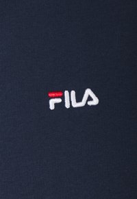 Tissu en coton bleu marine avec un logo "FILA" brodé en blanc et rouge, texture unie sans motifs ni accents supplémentaires.