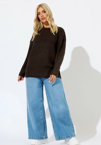 Brauner, gestrickter Pullover mit einem strukturierten Muster, kombiniert mit übergroßen, hellblauen Jeans. Verfügt über eine lockere Passform und lange Ärmel.