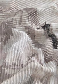 Pleated fabric in soft beige and gray tones, featuring a subtle sheen and abstract patterns. Texture is lightweight and flowing.