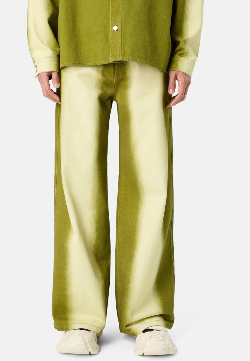 Pantalones verde oliva con un efecto degradado, diseño de pierna ancha, tejido suave y detalles de costura. Combinados con zapatillas blancas.