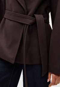 Cappotto marrone su misura con cintura, realizzato in tessuto testurizzato. Presenta maniche ampie e una silhouette pulita, completata da una finitura liscia.