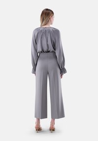 Graue Satinbluse mit elastischem Ausschnitt und geknöpften Ärmeln, kombiniert mit einer hoch taillierten, weit geschnittenen Hose in passendem Grau, getragen mit Absatzsandalen.