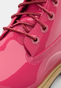 Bota de couro brilhante rosa patente com acabamento lustroso, cordões e ilhós castanhos. Apresenta uma sola em tom de tan contrastante e detalhes costurados.
