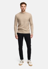 Maglione lavorato a maglia color beige chiaro con scollo rotondo, abbinato a pantaloni neri slim-fit e sneaker bianche con dettagli in marrone e nero.