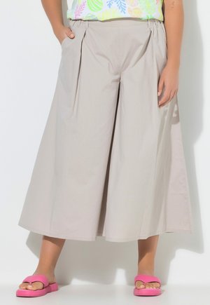 Beige cropped bukser med vide ben og plisseringer, båret med pink åbne sandaler og en farverig mønstret top.