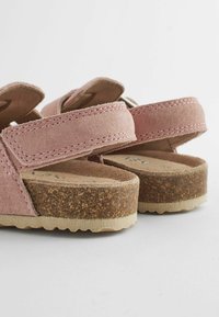 Sandales en velours rose avec des straps ajustables, semelle en liège texturé et design plat. Présentent des coutures visibles et une base brune contrastée.