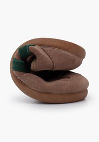 Sabot en daim brun avec une forme arrondie, présentant une texture douce et un accent vert sur le côté. Design plié pour un rangement facile.