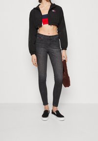 Černá zkrácená bunda, pruhovaný bralet, tmavé skinny džíny a černé nazouvací boty. Modelka drží hnědou chlupatou kabelku.