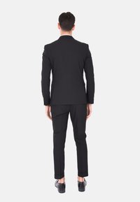Completo nero con giacca su misura e pantaloni slim, caratterizzato da una texture liscia, un design snello e sottili accenti in hardware dorato.