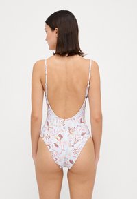 Maillot de bain une pièce aux couleurs pastel, décoré de motifs floraux. Présente un design à dos nu et de fines bretelles réglables. Texture de tissu lisse.