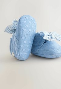 Pantofi pentru bebeluși de culoare albastru deschis, confecționați dintr-un material moale, cu modele în formă de inimă pe tălpi și panglici dungi în partea superioară. Prezintă o suprafață texturată.