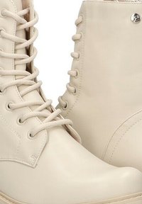 Botas de tobillo de imitación de cuero beige con puntera redonda, cordones en la parte delantera y pequeño detalle metálico. Textura suave y diseño minimalista.