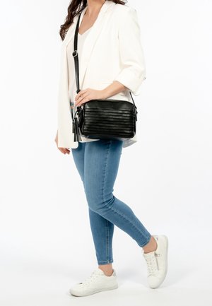 Sac à bandoulière en cuir noir avec des rayures verticales texturées. Il comporte une fermeture éclair, un accent avec un pompon et une bandoulière ajustable.