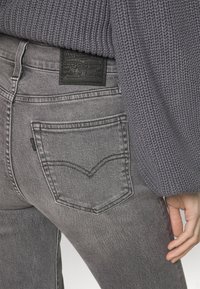 Jeans in denim grigio con vita alta, caratterizzati da un design distintivo della tasca posteriore curva e un'etichetta in pelle nera sulla cintura.