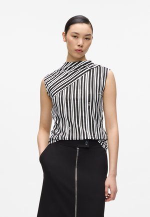 Mladá žena s uhladenými vlasmi, ktorá má na sebe čierno-biele pruhované tielko bez rukávov a čiernu sukňu so zipsom vpredu.