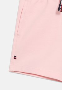 Απαλό ροζ ύφασμα σορτς με πλαϊνή τσέπη και μικρή κόκκινη, λευκή και μπλε ριγέ ετικέτα κοντά στο στρίφωμα σε λευκό φόντο.