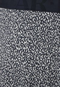 Legíny s černobílým abstraktním potiskem, s pevným černým páskem se vzorovaným logem. Měkká, elastická textura látky.