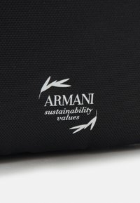Borsa tote nera in tessuto con superficie testurizzata. Caratterizzata da un marchio bianco "ARMANI valori di sostenibilità" e da accenti a foglia stilizzati.