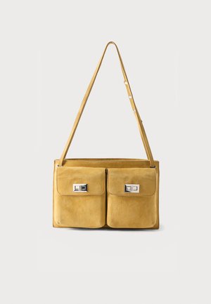 Garstyčių geltonos spalvos zomšinė petinė rankinė su dviem priekinėmis užsegamomis kišenėmis, stačiakampiais sidabriniais sukiojamais užraktukais ir reguliuojamu dirželiu.