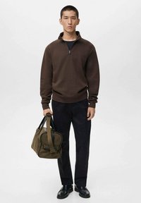 Pullover marrone con collo a zip, pantaloni neri e scarpe nere. Borsa duffel beige con dettagli neri tenuta a mano. Design semplice e strutturato.