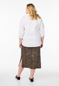 Chemise blanche à boutons avec les manches retroussées, associée à une jupe mi-longue en imprimé léopard avec des fentes latérales et des chaussures à enfiler marron foncé.