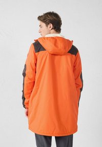 Oranje waterdichte jas met zwarte accenten, capuchon en een ontspannen pasvorm. Synthetisch materiaal, knielengte ontwerp en een gladde textuur.