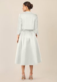 Biała, satynowa kurtka z rękawami do trzech quarto oraz plisowana spódnica do kolan. Gładka faktura oraz dopasowany krój podkreślają sylwetkę.