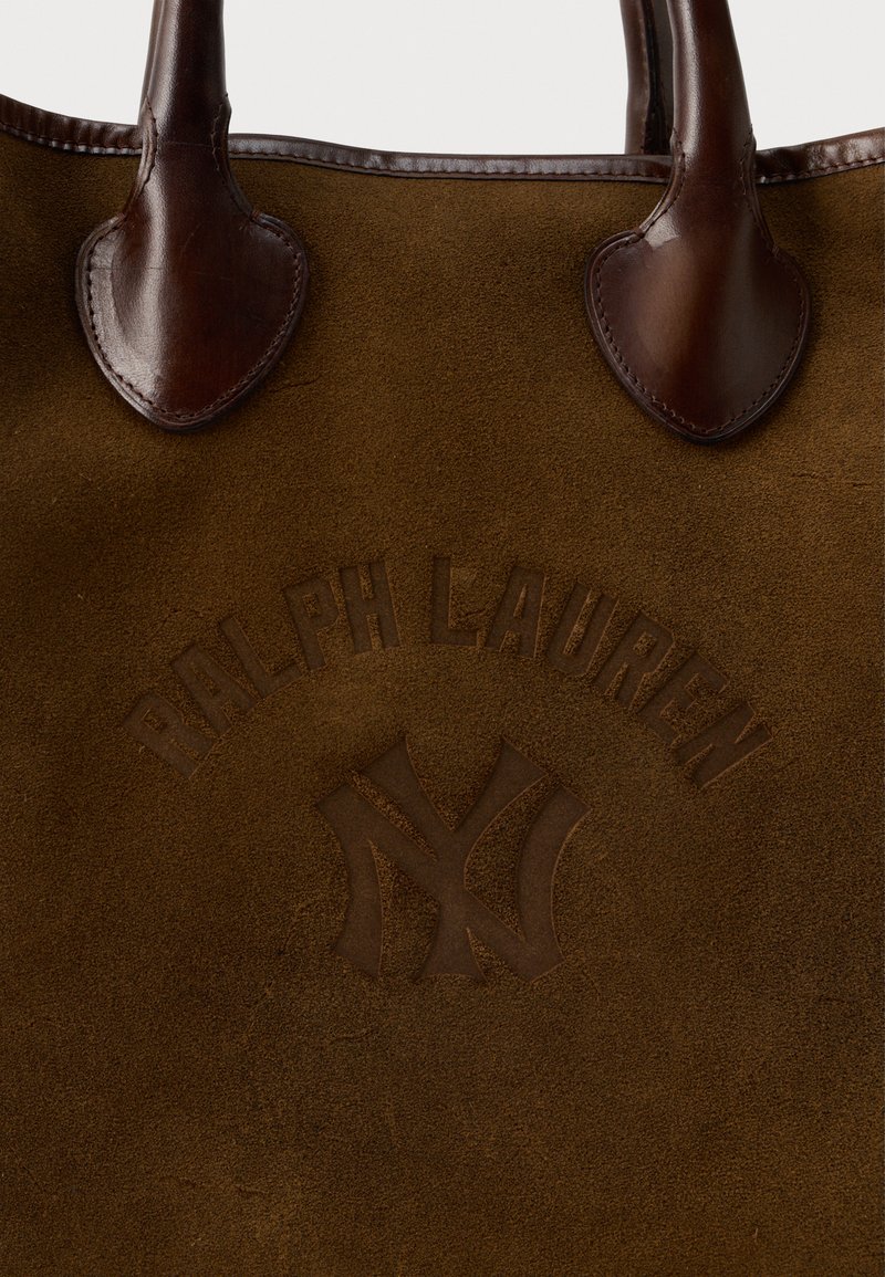 Brun ruskinds totebag med mørkebrune læderdetaljer, prægede logo med teksten "RALPH LAUREN" og NY-symbol, buede håndtag.