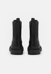 Botas de tobillo de cuero negro con un acabado suave, suelas de goma gruesas y lengüetas traseras; diseño elegante con herrajes mínimos.