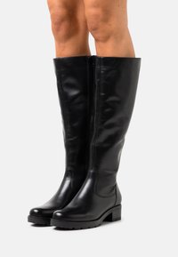 Bottes noires montantes en cuir lisse avec un bout arrondi, fermeture éclair latérale et un petit talon bloc, présentant une silhouette épurée et ajustée.