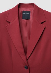 Blazer rosso con colletto a punte, singolo bottone nero e foderato in modo liscio. L'etichetta reca la scritta "CALLIOPE", taglia S. Il tessuto testurizzato conferisce struttura.