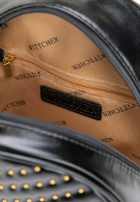 Czarna torebka wykonana z teksturowanego materiału, ozdobiona złotymi ćwiekami. Wewnątrz znajduje się beżowa podszewka z powtarzającym się wzorem "WITTCHEN" oraz zasuwana kieszeń.