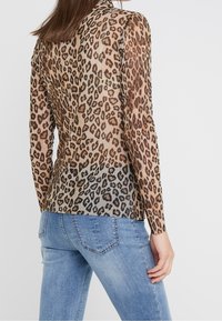 Průhledný top s dlouhým rukávem s leopardím potiskem, obsahující odstíny béžové a hnědé. Nosit s modrými džíny, ukazuje přiléhavý tvar.