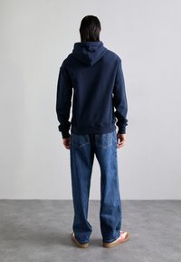 Navy sweatshirt with hood, paired with loose blue jeans. Casual shoes feature a pink accent. Focus on relaxed fit and soft texture.