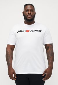 Witte katoenen t-shirt met een zwart "JACK & JONES" logo met een rode accent. Korte mouwen en een klassiek ronde hals ontwerp.