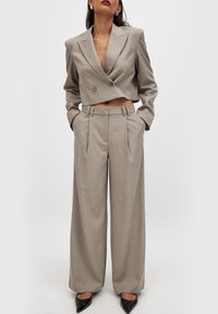 Blazer croisé gris clair à double boutonnage avec un pantalon large assorti ; les deux présentent une finition texturée et un design bien ajusté. Escarpins noirs à bout pointu.