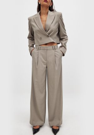 Blazer croisé gris clair à double boutonnage avec un pantalon large assorti ; les deux présentent une finition texturée et un design bien ajusté. Escarpins noirs à bout pointu.