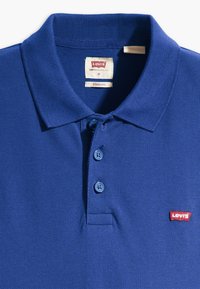 Camisa polo azul feita de tecido texturizado, com uma abertura de três botões e um pequeno logótipo vermelho da Levi's no lado esquerdo do peito.
