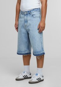 Pantalones cortos de mezclilla en azul claro, con dobladillos deshilachados y bolsillos, que presentan un corte clásico y una cintura con botones, combinados con zapatillas casuales.