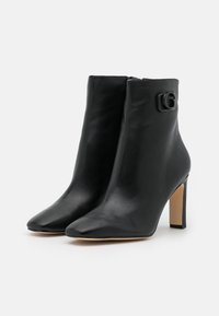 Svarta läderankelboots med spetsiga tår, en slimmad design och en blockklack i mellanhöjd. Har en svart detalj på sidan.