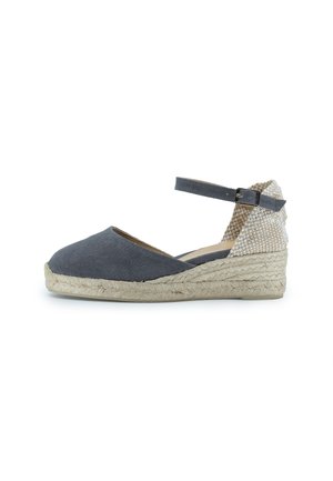 Espadrilles de lona gris con una suela de cuña de yute y una parte trasera de tela texturizada. Cuenta con una correa en el tobillo con un hebilla de metal.