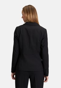 Čierny blazer s priliehavým strihom, klopovým golierom a gombíkovými manžetami. Hladká tkanina s strihom na mieru a jemnými švami.