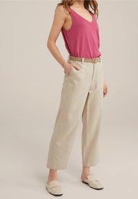 Rosa ärmlös topp med V-ringning, kombinerad med beige linnbyxor med fickor, midjeresår och ljusa slip-on skor.